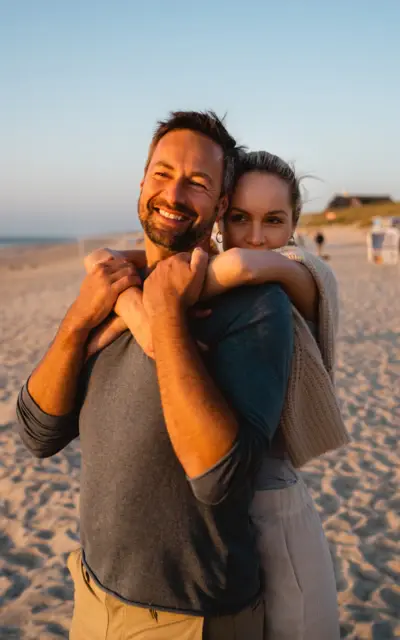 Ein Mann und eine Frau umarmen sich lächelnd am Strand.