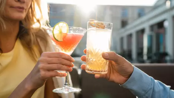 Eine Frau und ein Mann stoßen draußen mit einem Cocktail an.