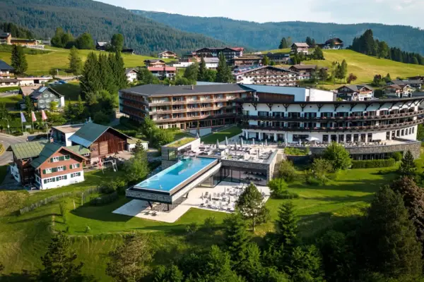 Gebäude mit einem Infinity-Pool inmitten eines Bergdorfes, umgeben von Bäumen und einer Landschaft mit Bergen.