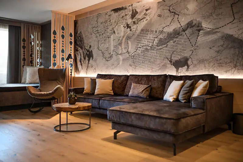 Gemütliches Wohnzimmer im alpinen Stil mit vielen Holzelementen, alpinen Details, kunstvoll gestalteter Tapete, Couch und Tisch.