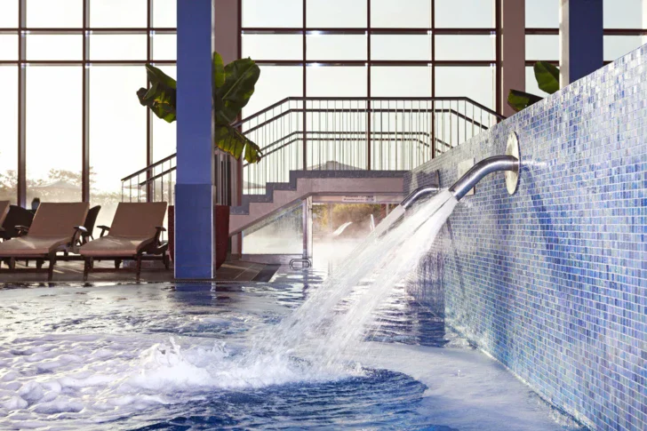 Swimmingpool mit Wasserfall im vor einer großen Fensterfront.