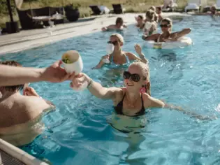 Im Pool entspannen Gäste mit Getränken in der Hand unter der strahlenden Sonne, genießen Sommerstimmung.