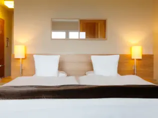 A hotel bed photographed from the front with two lights on the left and right above the bedside tables.