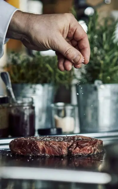 Eine Hand streut Salz auf ein Stück Fleisch.