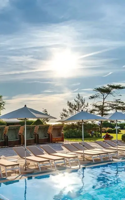 Pool mit Liegestühlen und Sonnenschirmen unter blauem Himmel.