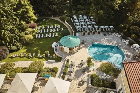 Idyllischer Wellnessbereich mit gepflegtem Garten, Liegestühlen, Sonnenschirmen und einem Außenpool. Ein Pavillon mit grünem Dach und Sitzgelegenheiten lädt zum Verweilen ein, umgeben von üppiger Vegetation.