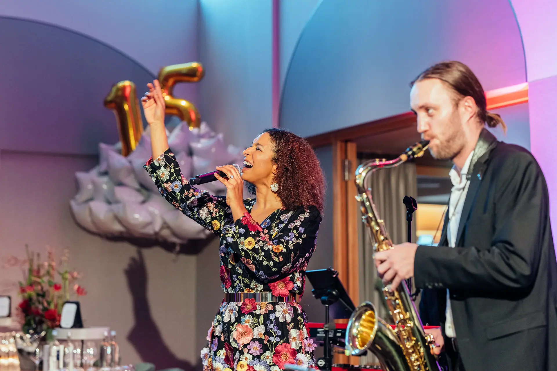 Eine Frau singt in ein Mikrofon, während ein Mann Saxophon spielt.