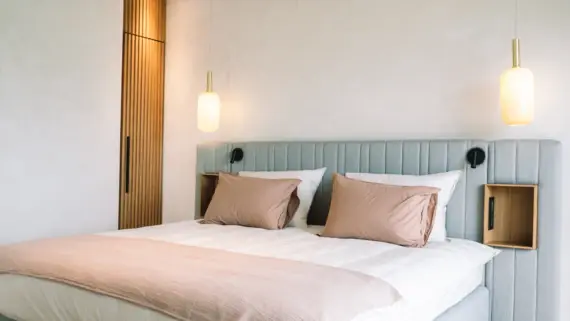 Interior view of a bedroom with a bed, pillows and two bedside lamps hanging from the ceiling.