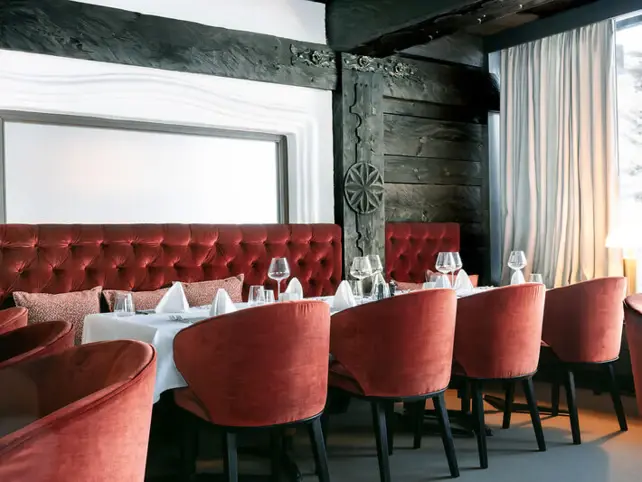 Elegantly furnished hotel dining room with a table, chairs, and curtains by a window.