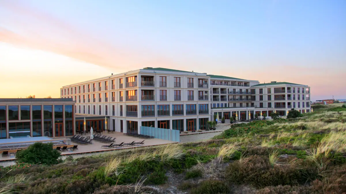 A-ROSA Hotel auf Sylt Gebäude mit Rasen und Stühlen im Freien bei Sonnenaufgang.