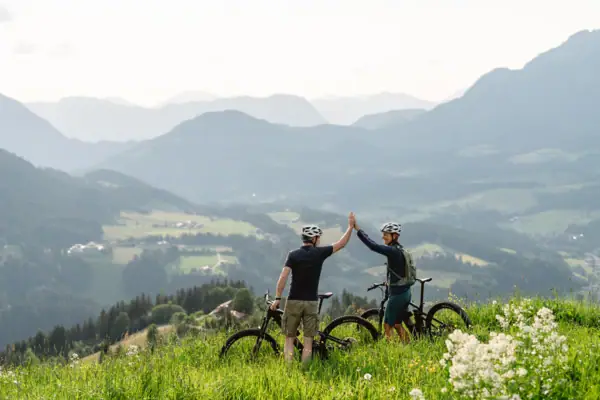 Zwei Personen stehen in einer Berglandschaft mit ihren fahhrädern und geben sich ein Highfive.