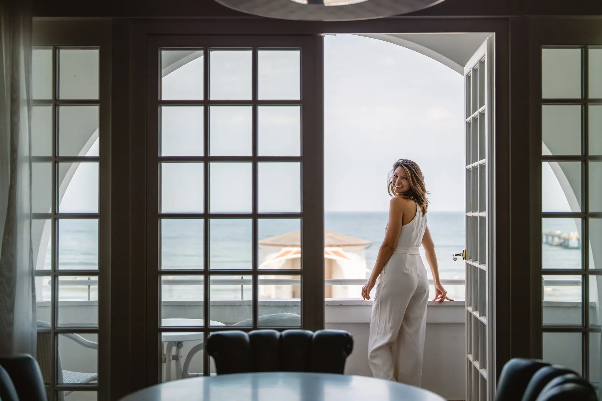 Eine Frau steht vor einem Fenster und blickt auf das Meer.
