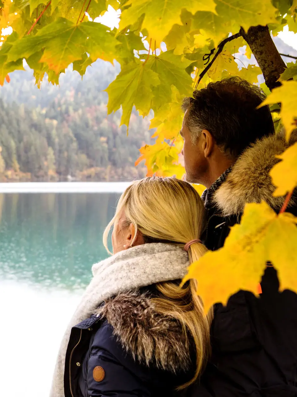 Ein Mann und eine Frau stehen unter einem Baum an einem See.