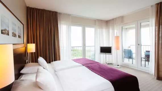 Ein Hotelzimmer mit großer Fensterfront und einem Balkon mit Meerblick.