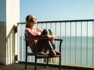 A woman sits on a chair on a balcony and enjoys the sun.