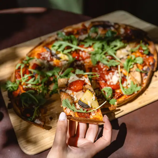Eine Hand hält ein Stück Pizza.
