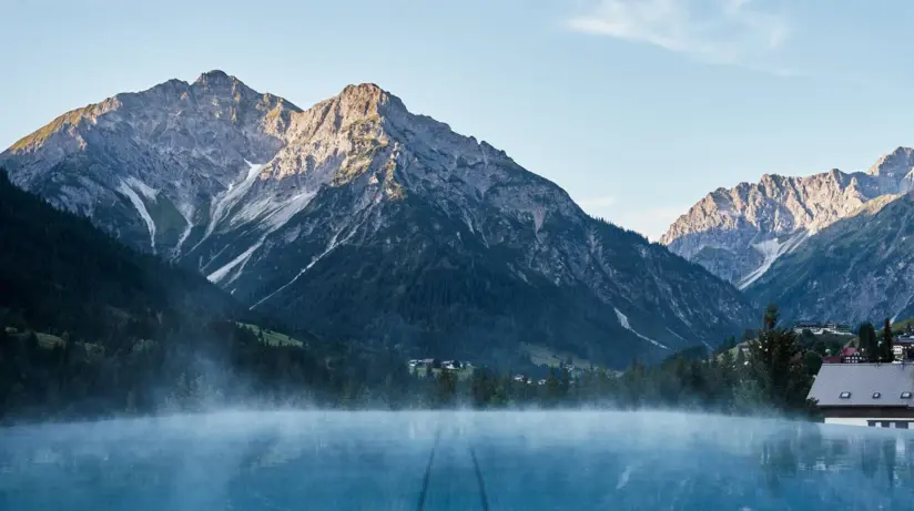 Blick auf einen Infinity-Pool in den Bergen mit schneebedeckten Bergen im Hintergrund.