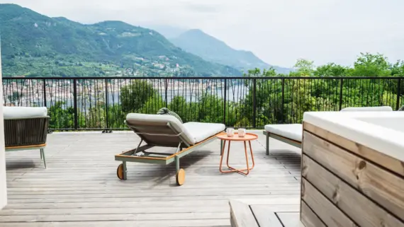 Terrasse mit Stühlen und einem Tisch, umgeben von Pflanzen und Bergblick.