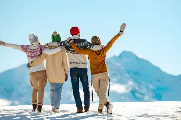 Four people stand in the snow with their backs to the camera, gazing at the snow-covered mountain landscape.