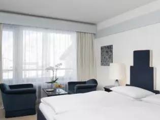 A hotel room with a blue bed and two blue armchairs.