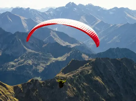 Person beim Paragliding über Berglandschaft.