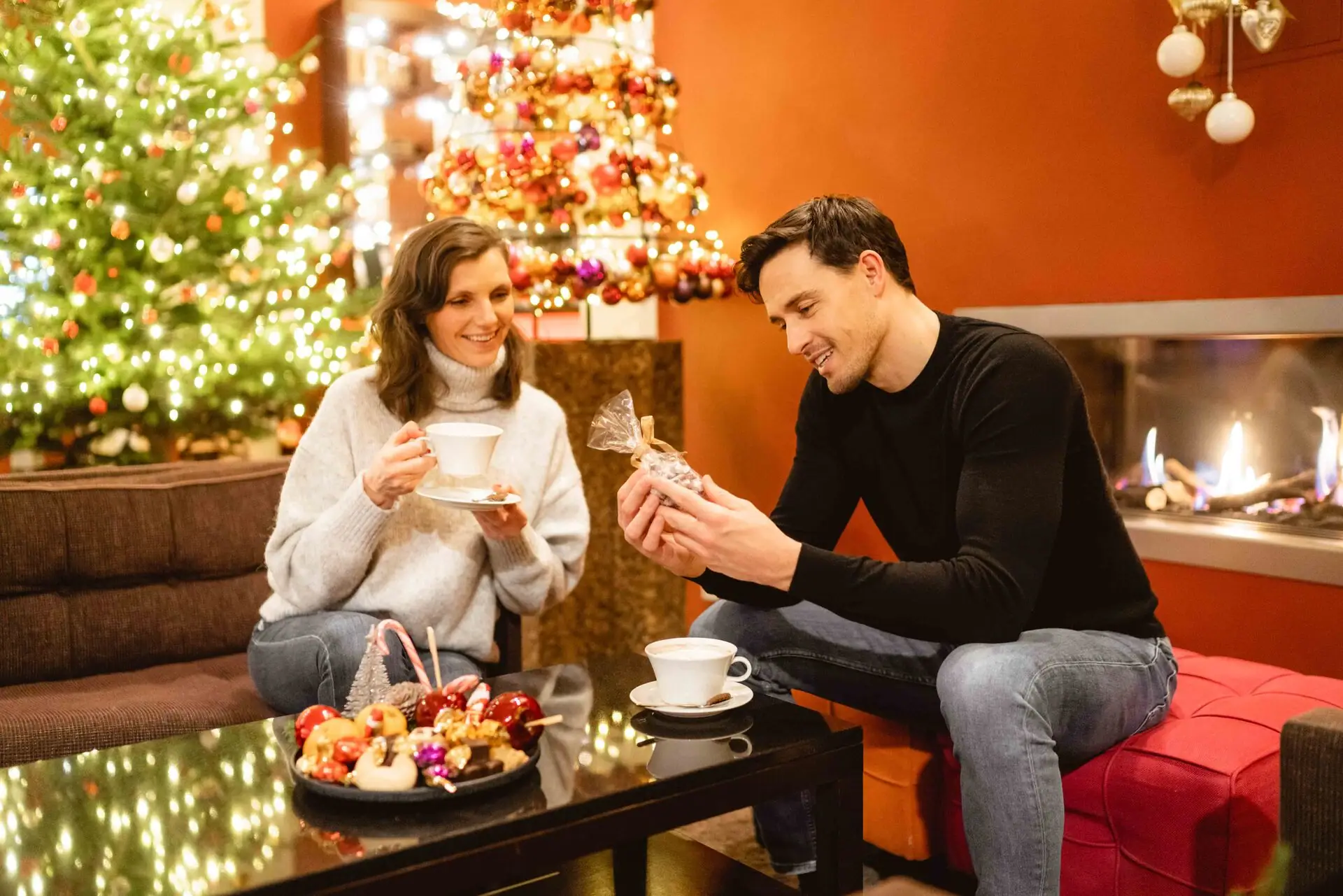 Ein Mann und eine Frau sitzen an einem Tisch mit Essen neben einem Weihnachtsbaum.