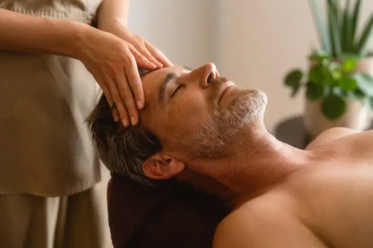 Ein Mann liegt auf einer Massage-Liege und bekommt den Kopf massiert.