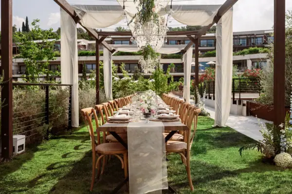 Hochzeitstafel unter einer mit Stoffbahnen und Blumen geschmückten Pergola im Garten des A-ROSA Gardasee.