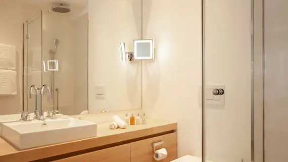 Ein modernes Badezimmer mit einem großem Waschtisch aus hellem Holz, auf dem ein eckiges weißes Waschbecken steht. Im Spiegelbild ist eine verglaste Duschkabine zu sehen.