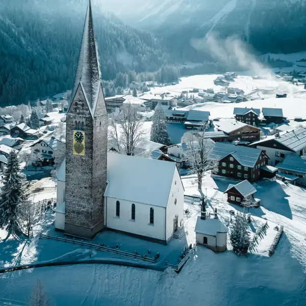 Kirche in einer verschneiten Stadt mit Bergen im Hintergrund.