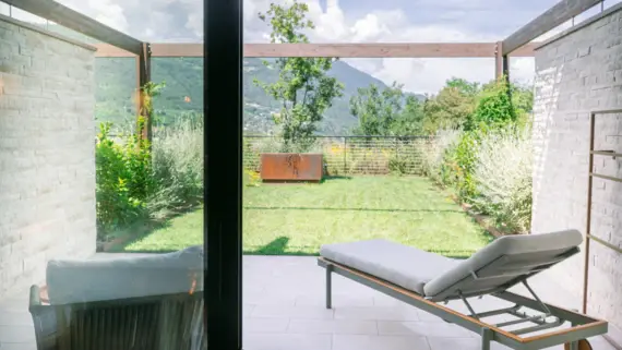 Lounge-Sessel im Freien mit Blick auf einen grünen Garten und Berge.