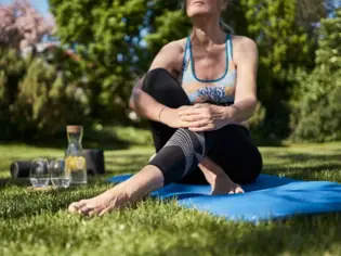 Frau sitzt beim Yoga auf einer Matte im Gras.