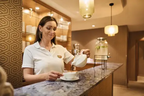 Woman in a spa area pouring tea into a cup.