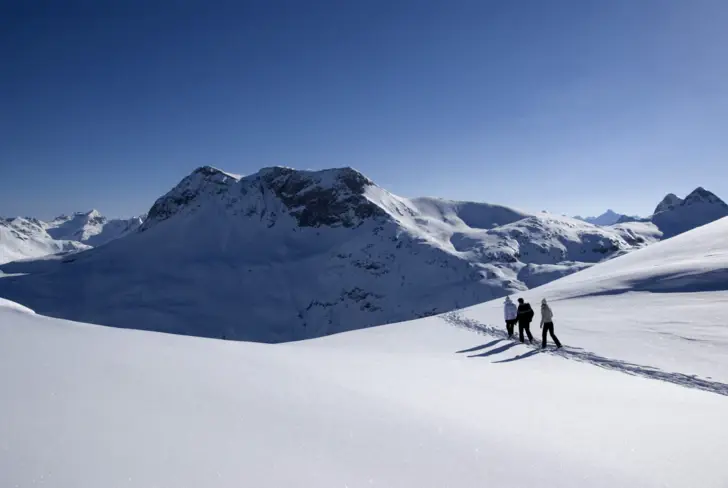 Three people hike through a snowy mountain landscape.