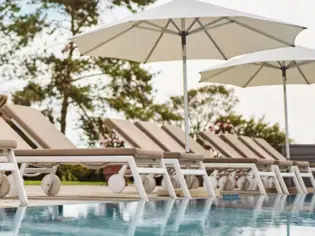 Sonnenliegen und Sonnenschirme am Pool, eingerahmt von sanftem Grün und strahlendem Himmel.