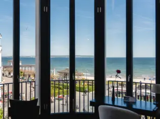 Blick vom Hotelzimmer mit Fenstern auf den sonnigen Strand und das Meer.