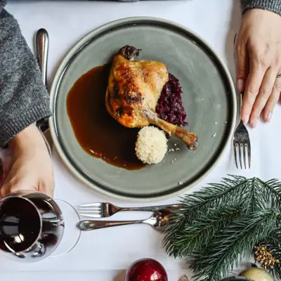 Eine Person hält ein Glas Wein über einem Teller mit Essen.