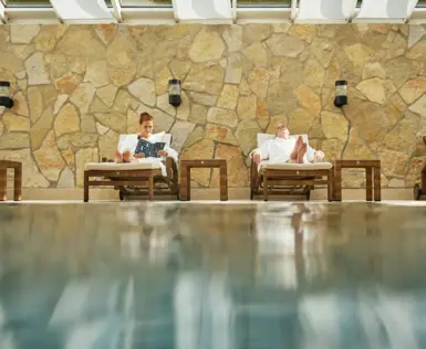 Zwei Personen in Bademänteln entspannen auf Liegen am Pool.