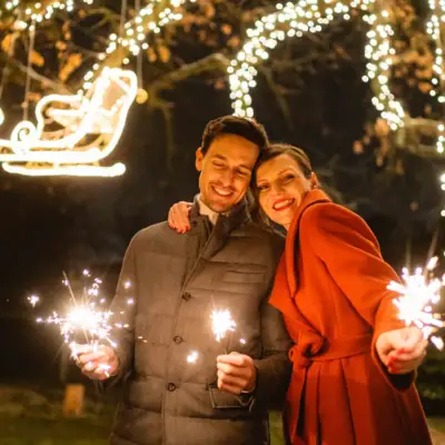 Ein Mann und eine Frau halten Wunderkerzen vor Lichterketten.