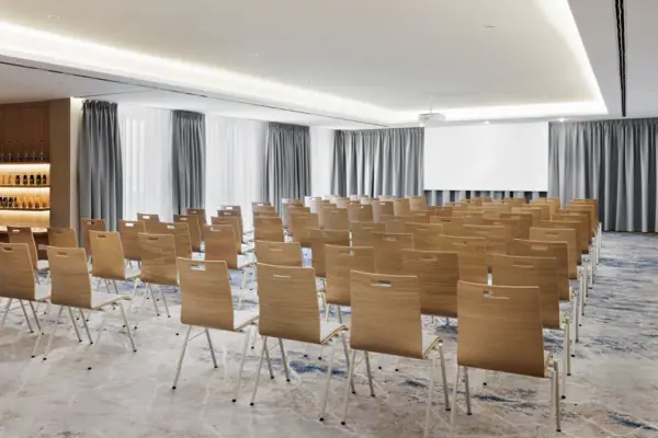 Konferenz 1 A-ROSA Tegernsee Der Konferenzraum 1 im A-ROSA Tegernsee mit Stuhlreihen und einem Beamer und einer Leinwand.