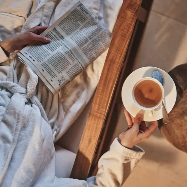 Person in einem Bademantel hält eine Tasse Tee und eine Zeitung in einem Innenraum.