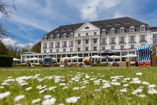 Außenansicht vom A-ROSa Travemünde mit Sonnenschirmen, Strandkörben und Gänseblümchen davor.