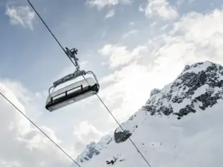Person riding a ski lift over a snowy mountain landscape.