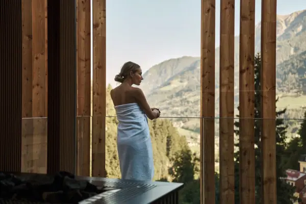 Eine Frau steht beim Day SPA im Straubinger Hotel in Bad Gastein im Handtuch vor einer Sauna und genießt den Ausblick auf die Berge.
