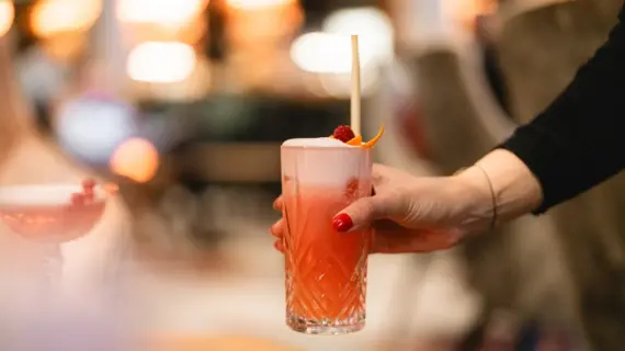 Eine Frauen Hand hält ein Glas mit einem roten Cocktail.
