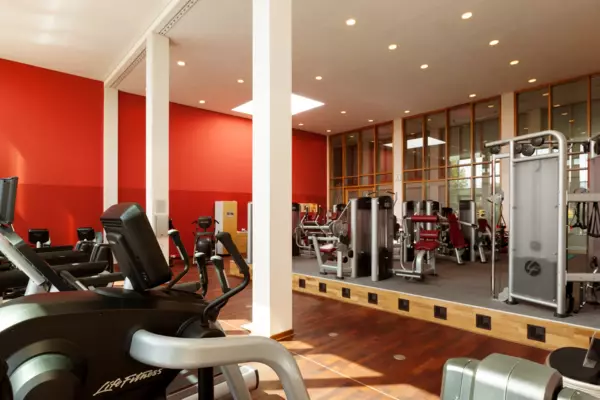 Ein Fitnessbereich mit roten Wänden und Holzboden stehen viele Sportgeräte verteilt. 