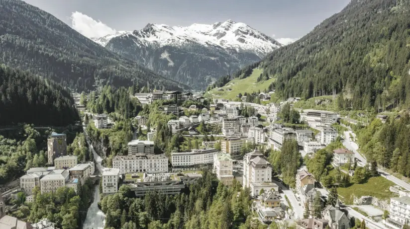 Stadt in den Bergen mit umliegenden bewaldeten Hängen und schneebedeckten Gipfeln.