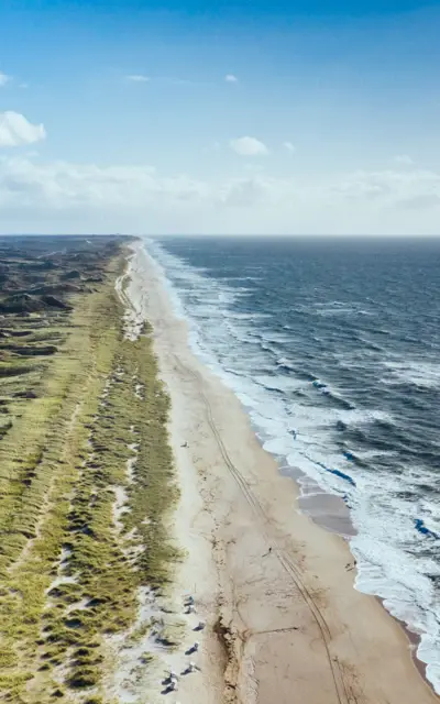 Langer Strand mit heranrollenden Wellen.