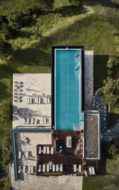 Pool mit Liegestühlen auf der Dachterrasse eines Gebäudes, umgeben von Gras und Pflanzen, aufgenommen aus der Vogelperspektive.