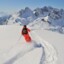 Ein Skifahrer in roter Kleidung mit einem Rucksack auf dem Rücken fährt durch Tiefschnee.